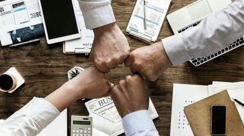 four hands joining on top of desk