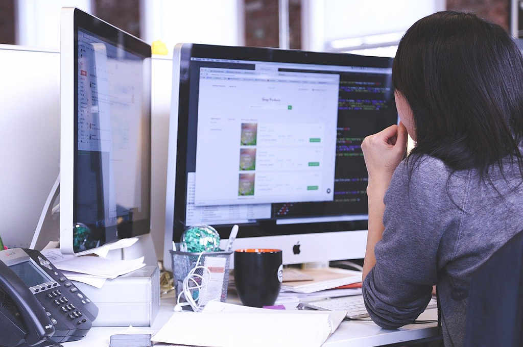 woman on desk watching two monitors with websites